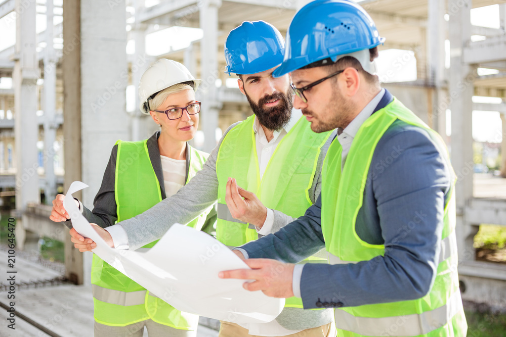 Mixed group of young engineers or business partners at construction site, working together on building's blueprint. Architecture and teamwork concept. Mixed group of young engineers or business partners at construction site, working together on building's blueprint. Architecture and teamwork concept.