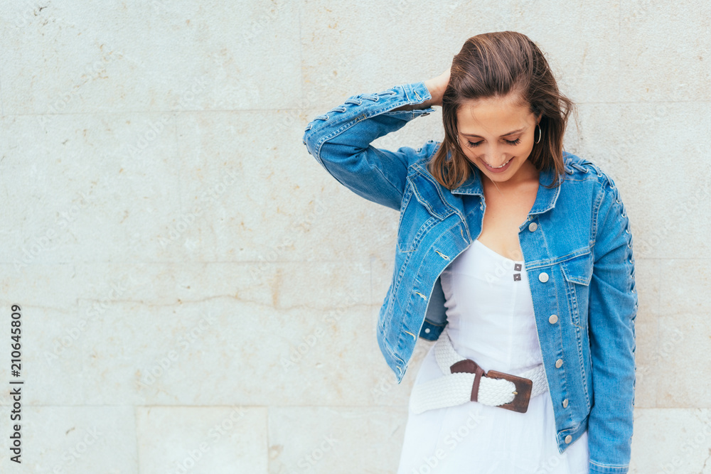 lächelnde frau mit jeansjacke und weißem kleid schaut nach unten lächelnde frau mit jeansjacke und weißem kleid schaut nach unten