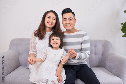 Portrait of beautiful young parents and their cute little daughter hugging, looking at camera and smiling