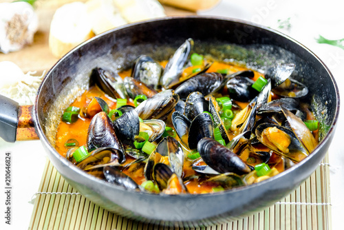 Delicious seafood mussels with red sauce and green onions in a pan