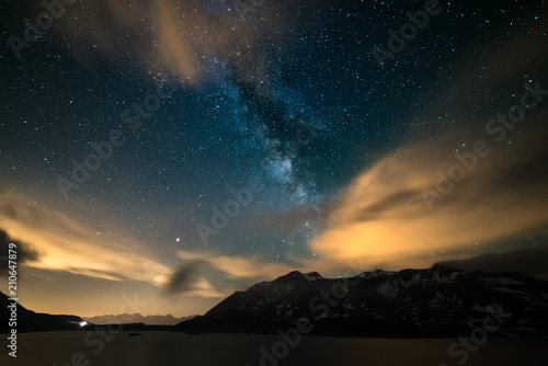 Astro night sky, Milky way galaxy stars over the Alps, stormy sky, motion clouds, snowcapped mountain range and lake © fabio lamanna