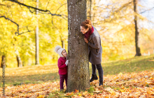 family, season and people concept - happy mother and little daughter at tree trunk playing in autumn park