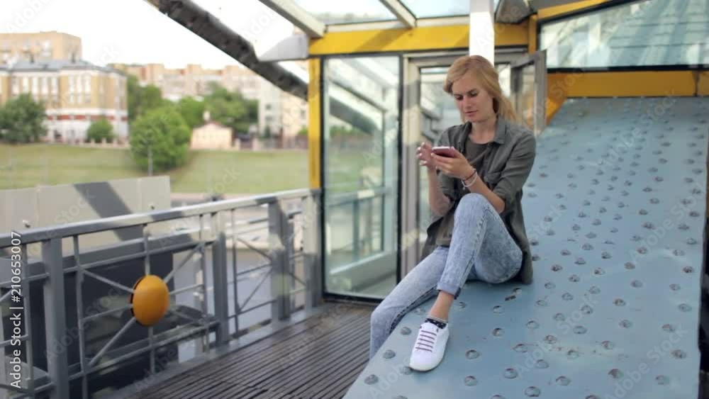 beautiful woman with a phone sits on an iron construction beautiful woman with a phone sits on an iron construction