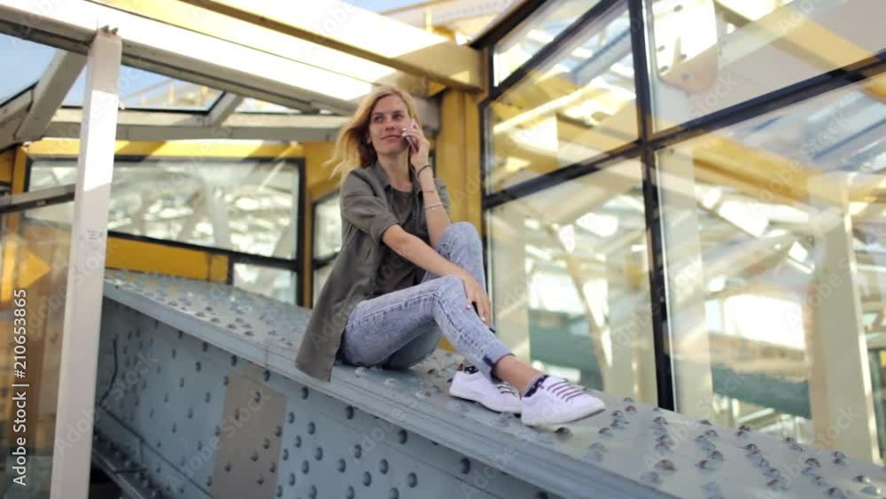 girl talking on the phone while sitting on an iron bridge construction girl talking on the phone while sitting on an iron bridge construction