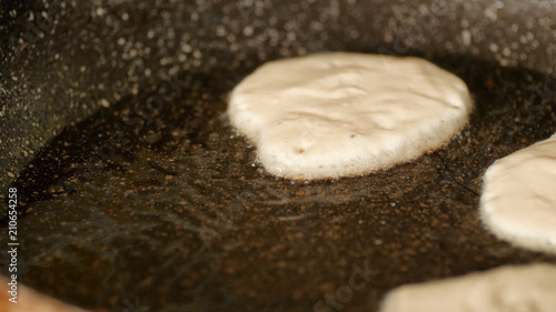 Closeup view pouring fresh white pancake dough mixture into preheat cast iron pan with vegetable oil at home