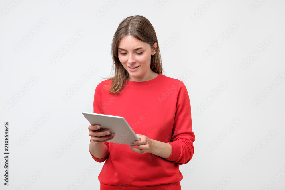 Elegant young woman in red sweater using tablet, looking at screen Elegant young woman in red sweater using tablet, looking at screen