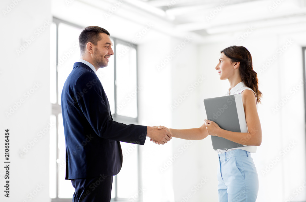 business people, partnership and cooperation concept - happy smiling businesswoman with folder and businessman shake hands at office