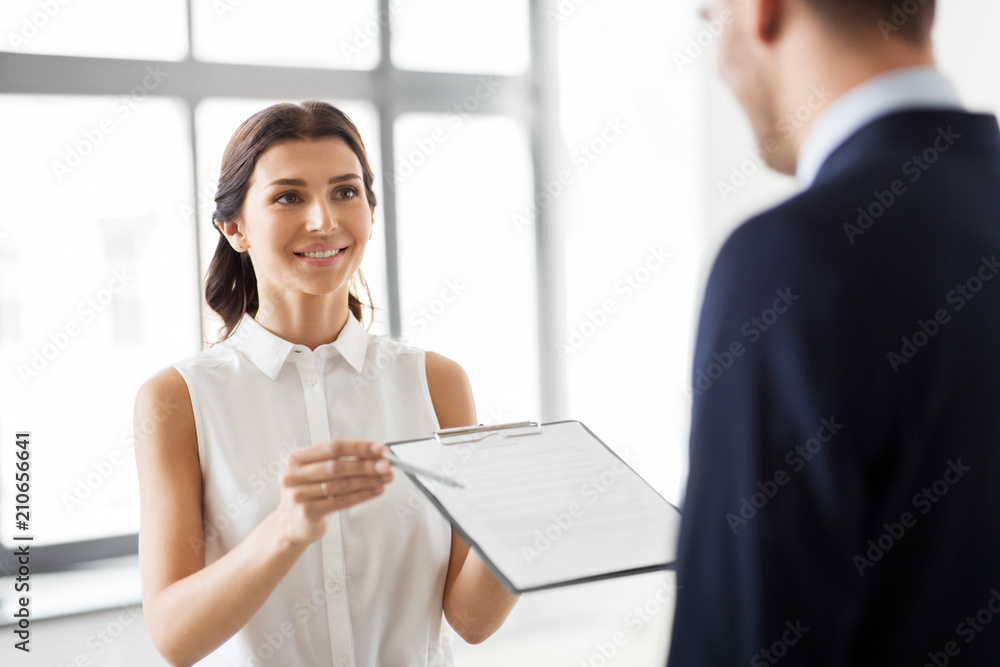 real estate business, sale and people concept - female realtor with clipboard showing contract document to customers at new office room real estate business, sale and people concept - female realtor with clipboard showing contract document to customers at new office room
