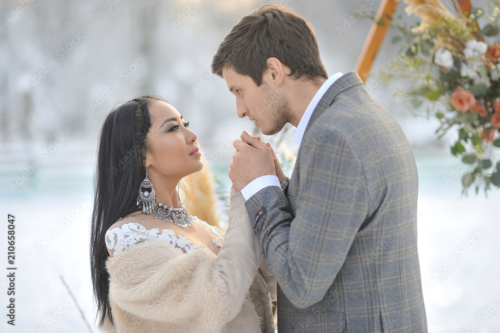 Naklejka premium Winter wedding European bridegroom and Asian bride
