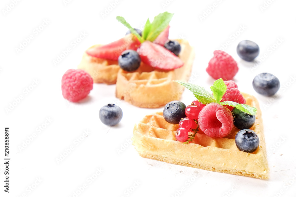 Heart shape belgium waffles with assorted berries mix, strawberry, blueberry, raspberry and red currant decorated with mint leaf on white ceramic plate. Close up, copy space, background, top view. Heart shape belgium waffles with assorted berries mix, strawberry, blueberry, raspberry and red currant decorated with mint leaf on white ceramic plate. Close up, copy space, background, top view.