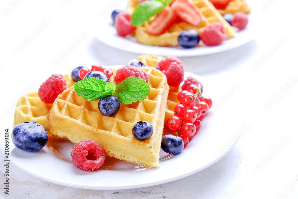 Heart shape belgium waffles with assorted berries mix, strawberry, blueberry, raspberry and red currant decorated with mint leaf on white ceramic plate. Close up, copy space, background, top view. Heart shape belgium waffles with assorted berries mix, strawberry, blueberry, raspberry and red currant decorated with mint leaf on white ceramic plate. Close up, copy space, background, top view.