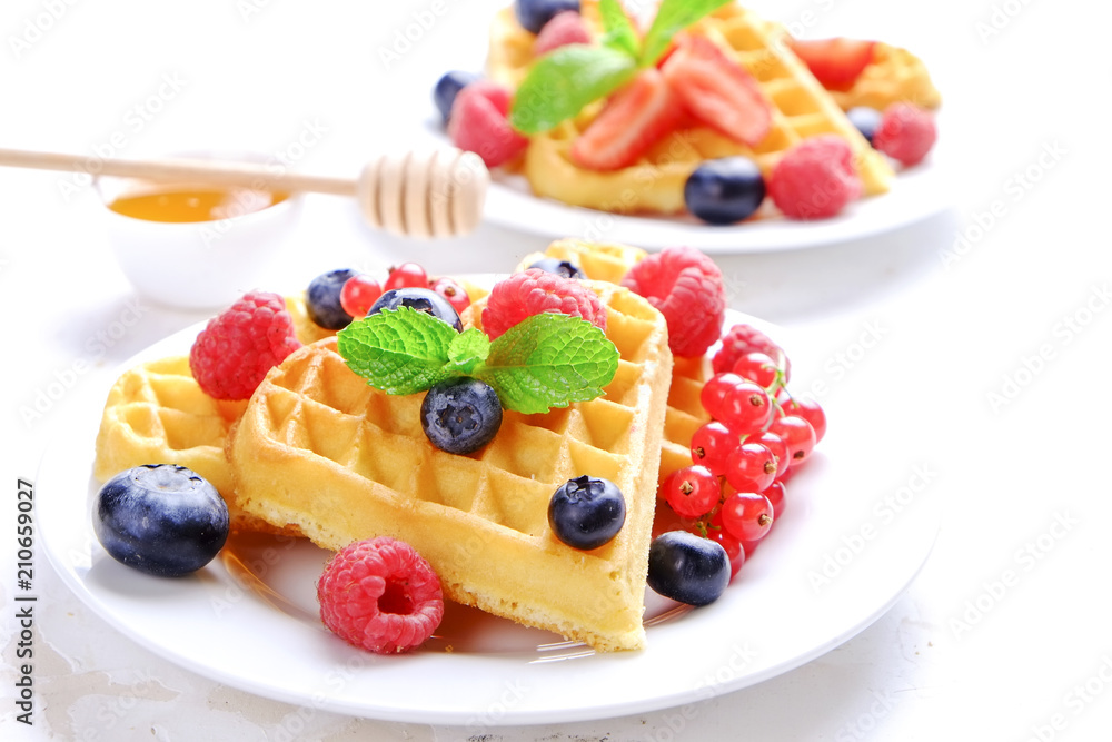 Heart shape belgium waffles with assorted berries mix, strawberry, blueberry, raspberry and red currant decorated with mint leaf on white ceramic plate. Close up, copy space, background, top view.