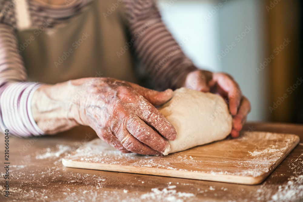 An unrecognizale senior woman kneading dough in the kitchen at home.
