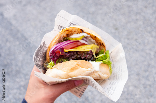 Hand of a young man holding an organic vegan burger with seitan patty in his hand during a street food festival