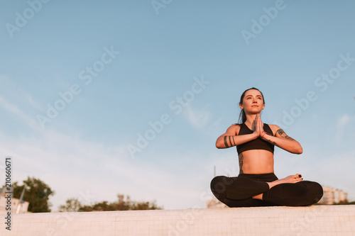 Beautiful lady sitting in lotus pose and dreamily looking aside. Young woman in black sporty top and leggings meditating while practicing yoga