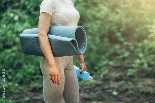 Fitness Woman Preparing for Yoga in the Early Morning Park. Wearing Stylish Sport Outfit. Blue Bottle of Water and Yoga Mat. Healthy Lifestyle.