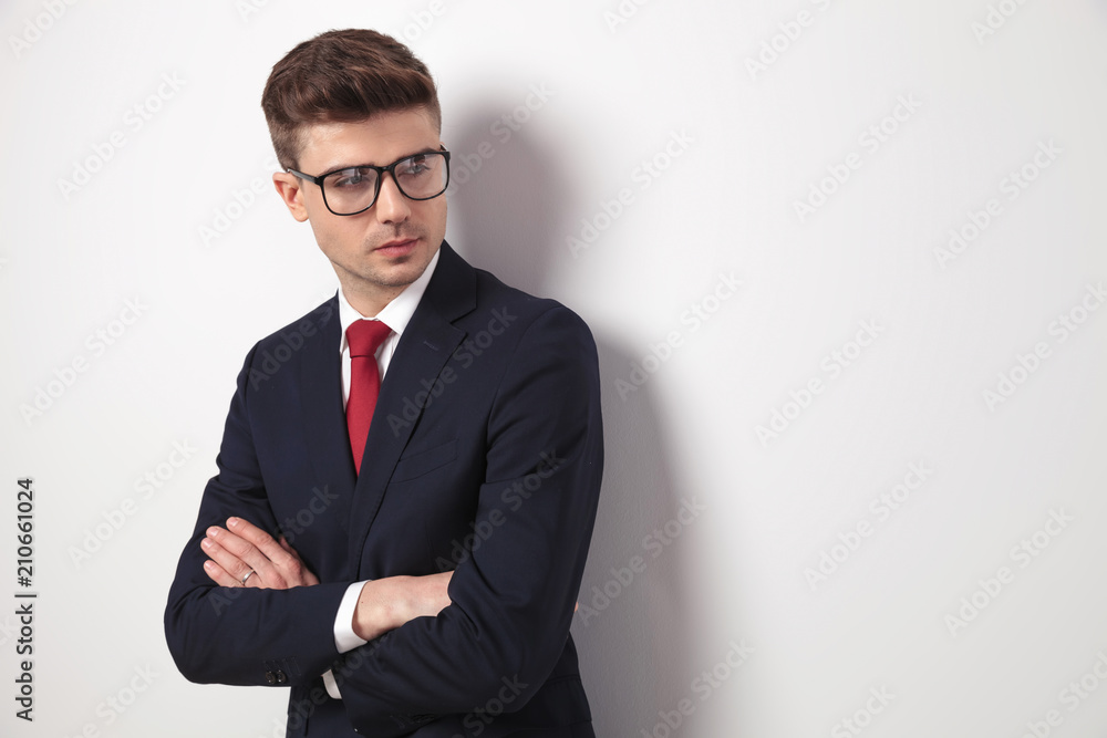 young businessman with glasses and arms folded looks to side - obrazy, fototapety, plakaty 