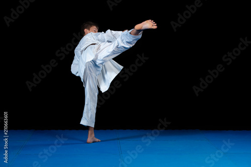 Young boy training karate on black background