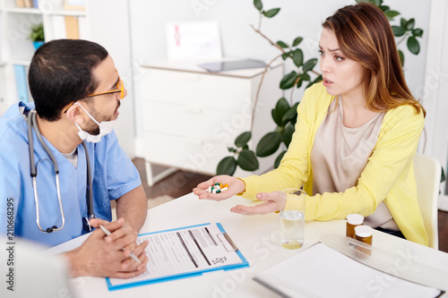 Tableau sur toile Portrait of worried  young woman sitting at desk in doctors office and holding h