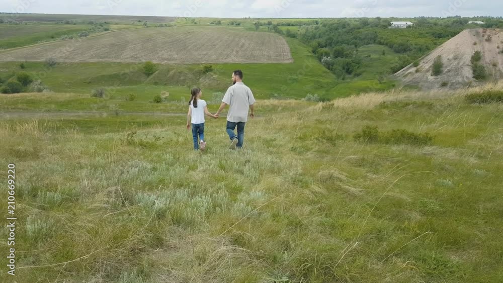 daughter and father play in nature. a bearded man with a daughter walking on the hills on a summer day, holding hands. daughter and father play in nature. a bearded man with a daughter walking on the hills on a summer day, holding hands.