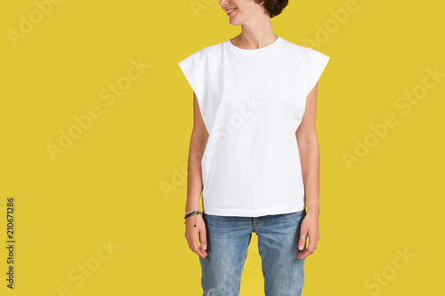 Studio shot of unrecogizable young female hipster dressed in oversize white t-shirt posing indoors at blank yellow wall with copy space for your text or advertising content photo