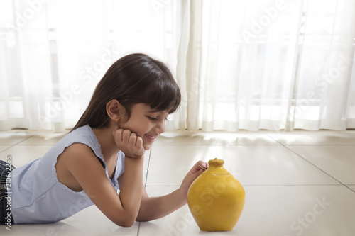 Photography Little girl lying on floor and putting coin in clay piggy bank