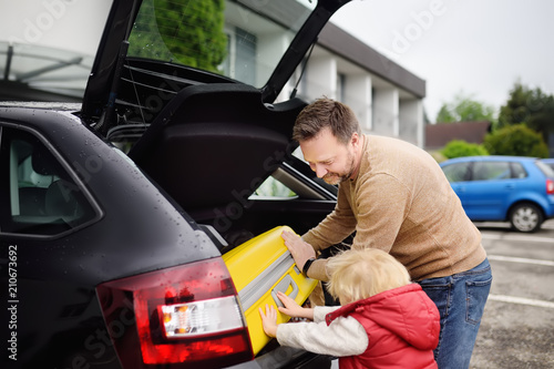 Handsome man and his little son going to vacations, loading their suitcase in car trunk