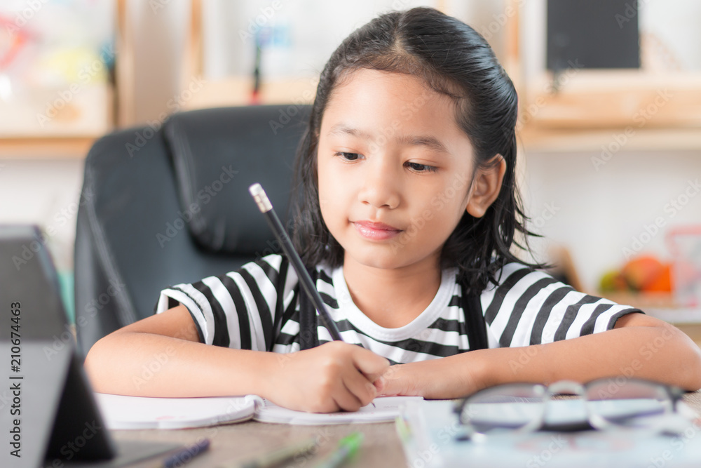 Asian little girl doing homework and pointing finger on wooden table select focus shallow depth of field Asian little girl doing homework and pointing finger on wooden table select focus shallow depth of field