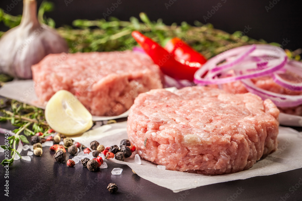 Cutlets from raw minced pork, lamb, veal or beef on parchment. Nearby spices and vegetables. On a black and wooden background. Copy space