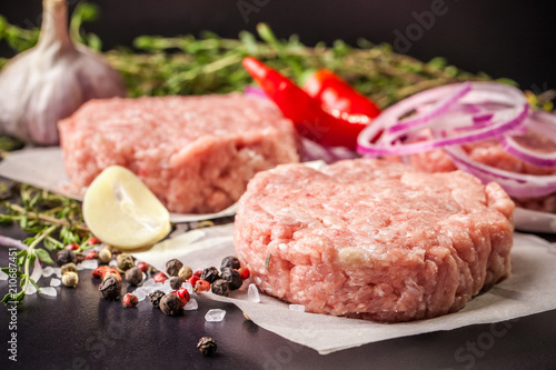 Cutlets from raw minced pork, lamb, veal or beef on parchment. Nearby spices and vegetables. On a black and wooden background. Copy space