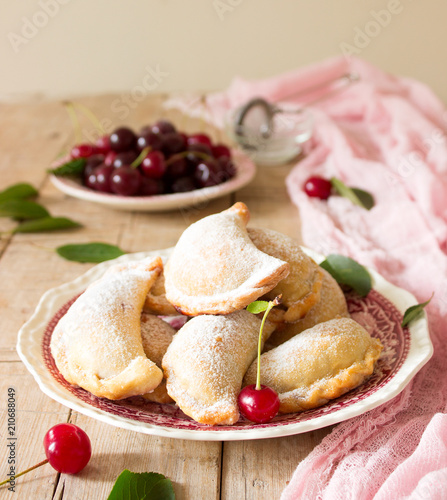 Pies with cherries, sprinkled with powdered sugar and berries of fresh cherries on a wooden surface.