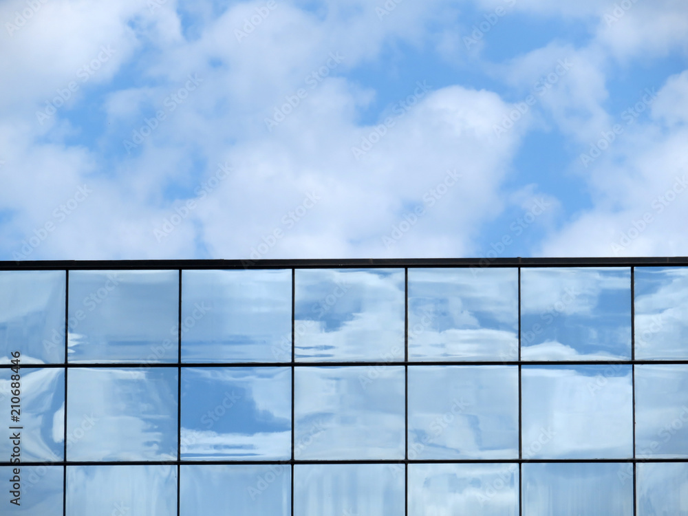 Glass facade of the building with the reflection of clouds against the blue cloudy sky. The top of a skyscraper, beautiful architecture background Glass facade of the building with the reflection of clouds against the blue cloudy sky. The top of a skyscraper, beautiful architecture background