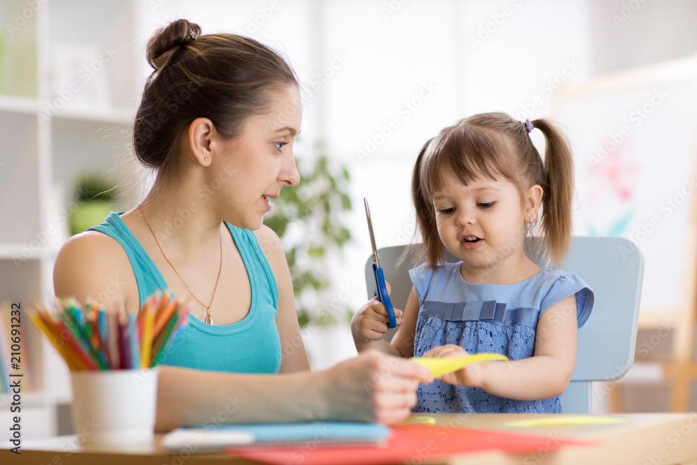 Mother helping her child daughter to cut colored paper Mother helping her child daughter to cut colored paper