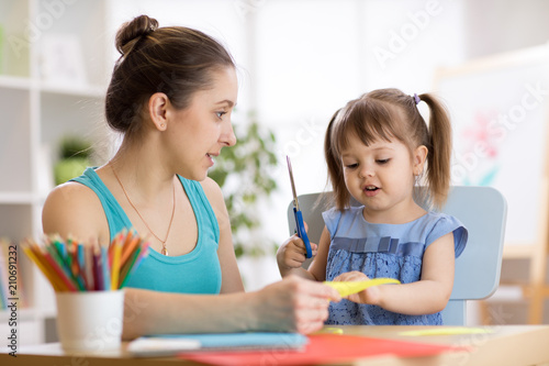 Mother helping her child daughter to cut colored paper