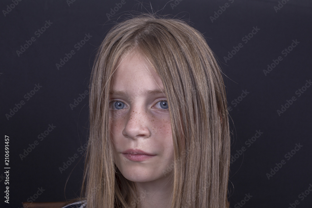 Naklejka premium Beautiful blond young girl with freckles indoors on black background, closeup portrait