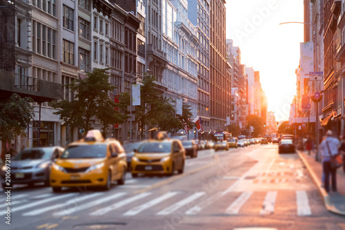 Canvas Print Sunlight shines down a busy street in New York City with taxis stopped at the in