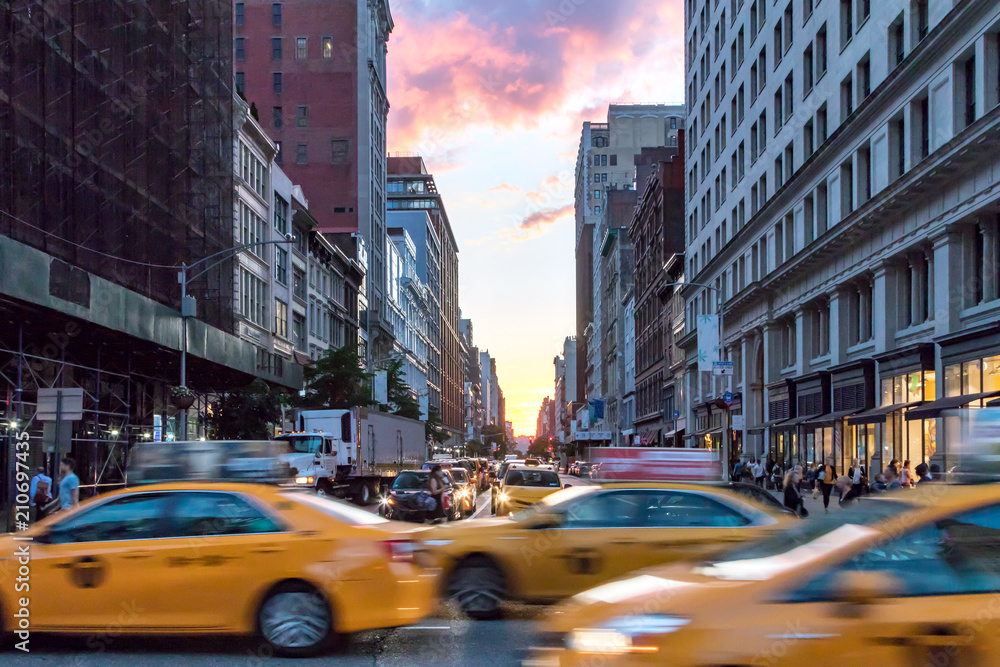 Naklejka premium Żółte taksówki przyśpieszają w dół Broadway podczas godziny szczytu na Manhattanie, Nowy Jork z kolorowym zachodem słońca niebo w tle