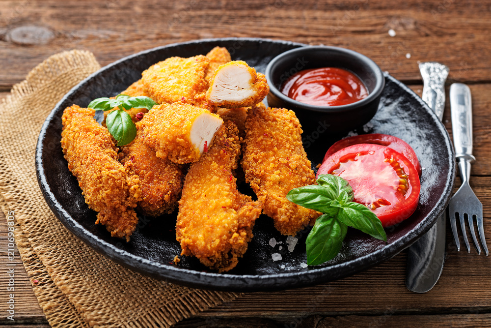 Fototapeta premium Delicious crispy fried breaded chicken breast strips with ketchup on black plate.