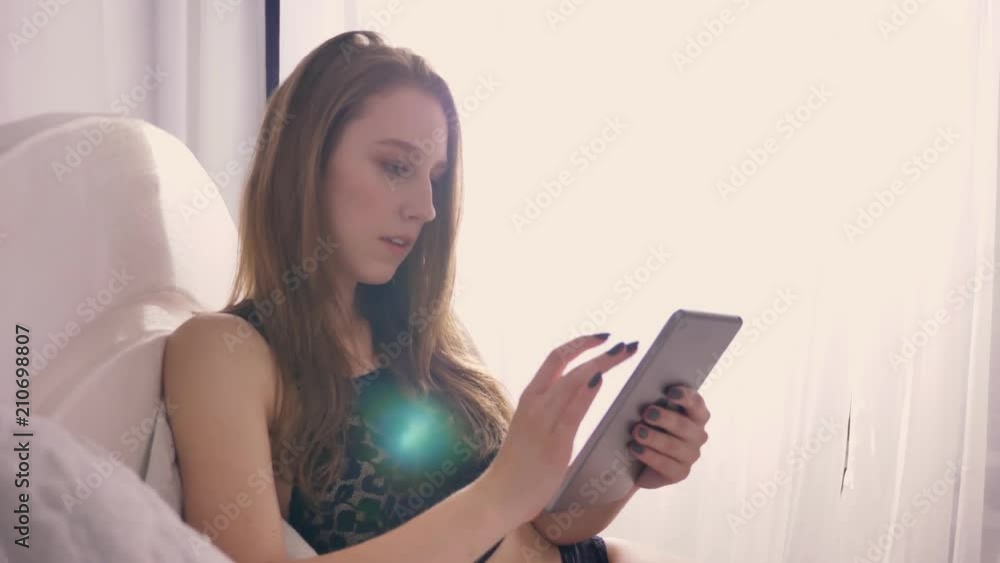 Young sexy girl in lingerie is laying on bed and watching tablet, sunlight, relax concept, flirt concept, communication concept Young sexy girl in lingerie is laying on bed and watching tablet, sunlight, relax concept, flirt concept, communication concept