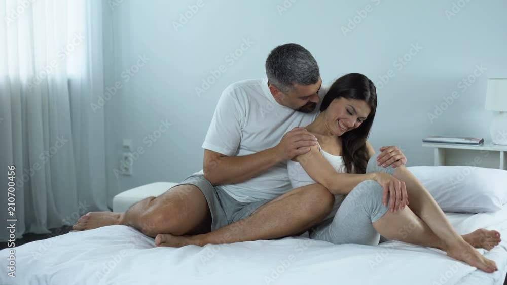 Man gently stroking shoulders of his beloved, couple speaking sitting on bed Man gently stroking shoulders of his beloved, couple speaking sitting on bed