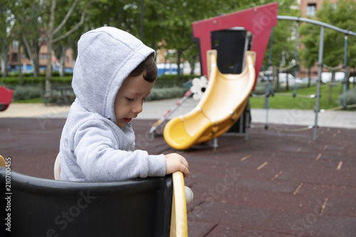 Child under two years playing in the park with a gray jacket and blue pants.
