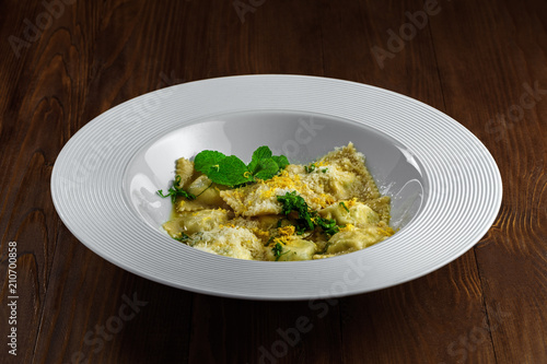 Ravioli filled with ricotta, mint and grated lemon rind on a rustic wooden table. Classic Italian cuisine pasta meal in a soup plate.