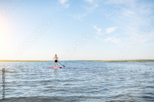 Man paddleboarding on the lake during the morning light, wide landscape view with blue water and sky © rh2010