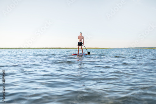 Man paddleboarding on the lake during the morning light, wide landscape view with blue water and sky