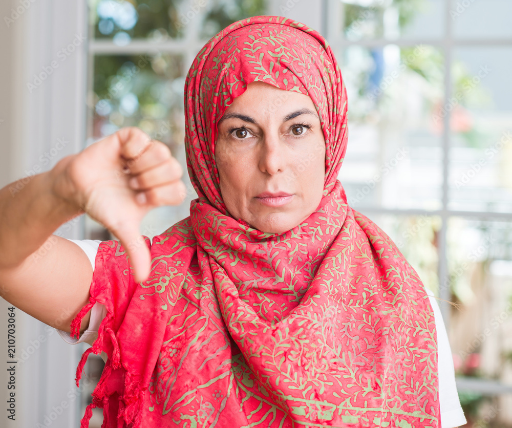 Middle aged muslim woman wearing hijab with angry face, negative sign showing dislike with thumbs down, rejection concept Middle aged muslim woman wearing hijab with angry face, negative sign showing dislike with thumbs down, rejection concept