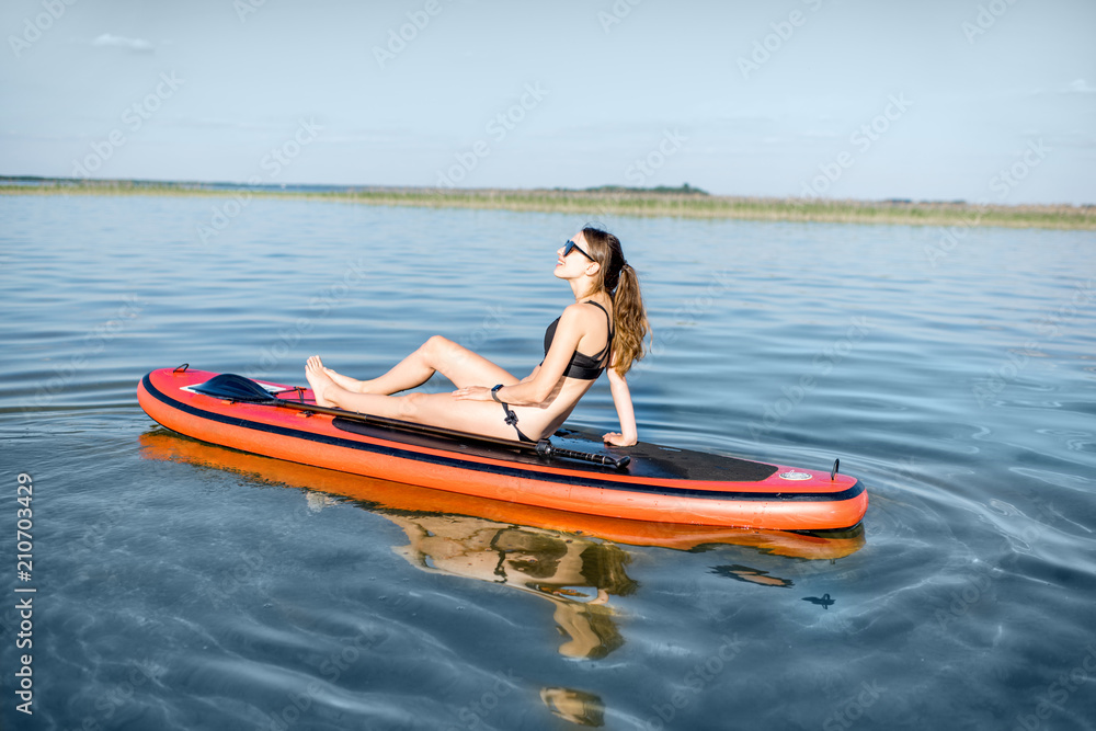 Fototapeta premium Młoda kobieta relaks na paddleboard, ciesząc się spokojną wodą podczas zachodu słońca