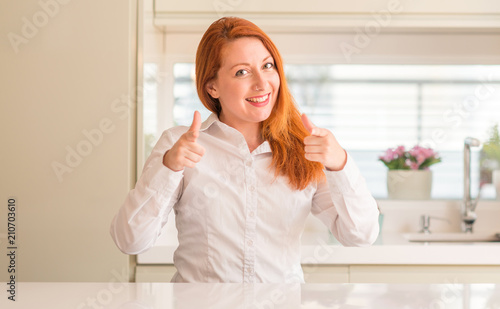 Redhead woman at kitchen pointing fingers to camera with happy and funny face. Good energy and vibes.