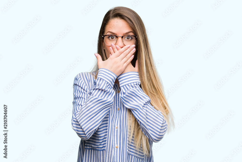 Beautiful young woman wearing elegant shirt and glasses shocked covering mouth with hands for mistake. Secret concept.