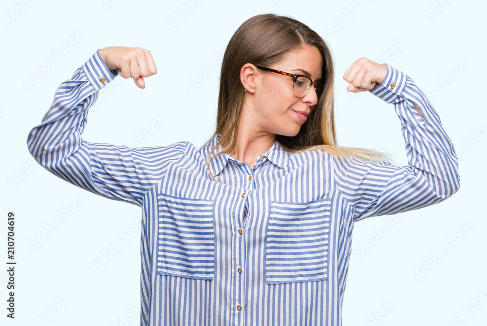 Beautiful young woman wearing elegant shirt and glasses showing arms muscles smiling proud. Fitness concept. Beautiful young woman wearing elegant shirt and glasses showing arms muscles smiling proud. Fitness concept.