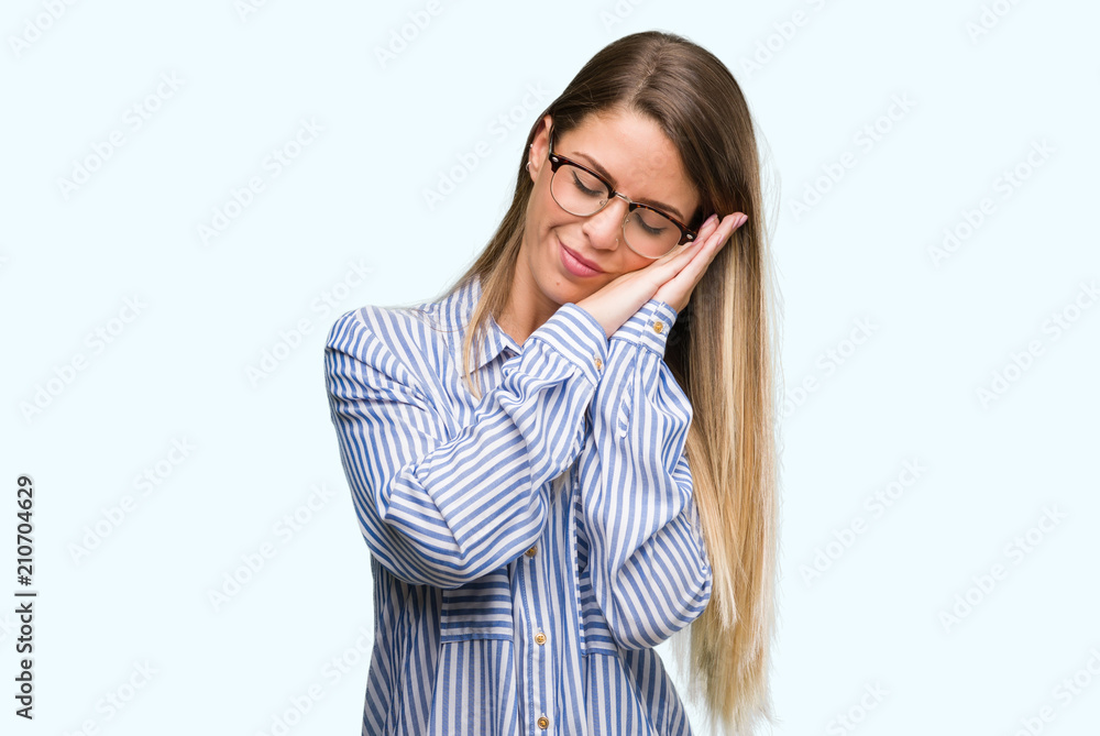 Beautiful young woman wearing elegant shirt and glasses sleeping tired dreaming and posing with hands together while smiling with closed eyes.